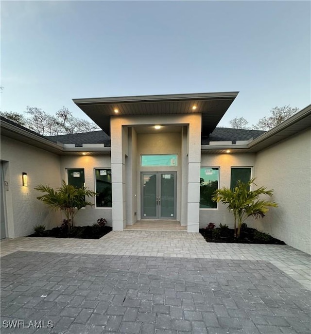 entrance to property featuring stucco siding, french doors, and roof with shingles