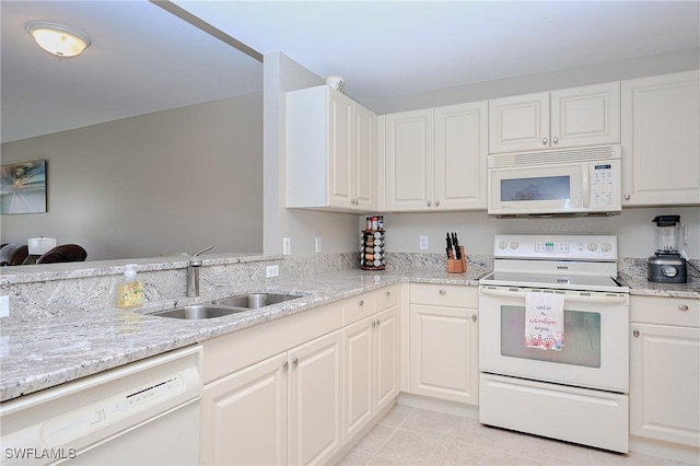 kitchen with a sink, light stone counters, white appliances, white cabinets, and light tile patterned floors