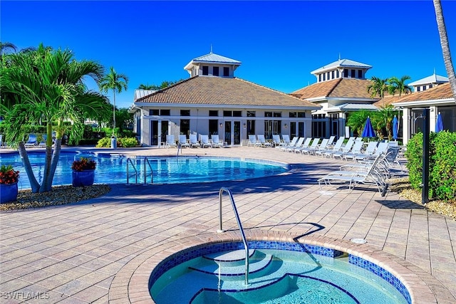 community pool with a patio area, fence, and a hot tub