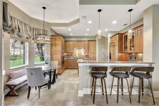 9293 Menaggio Ct Unit 102, Naples, FL 34114 - kitchen with light stone countertops, under cabinet range hood, built in appliances, a peninsula, and brown cabinetry