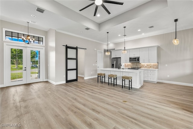 kitchen with a kitchen island with sink, stainless steel appliances, light countertops, a barn door, and a kitchen breakfast bar