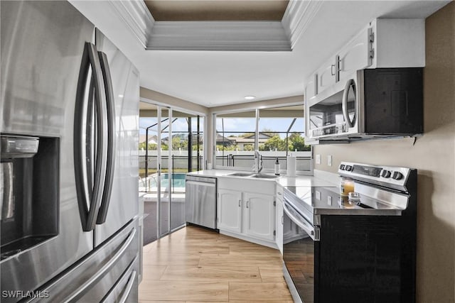 kitchen with a sink, white cabinetry, appliances with stainless steel finishes, crown molding, and a raised ceiling