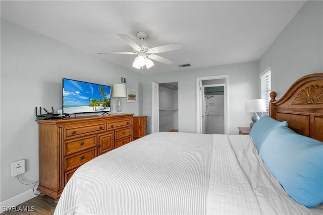 bedroom with wood finished floors, a ceiling fan, visible vents, baseboards, and a walk in closet