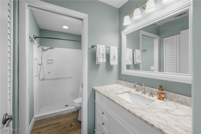 full bathroom with visible vents, toilet, a tile shower, wood finished floors, and vanity