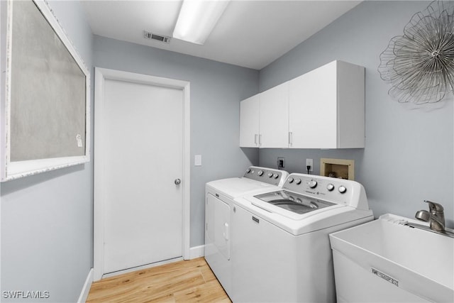 clothes washing area with visible vents, washing machine and dryer, light wood-type flooring, cabinet space, and a sink