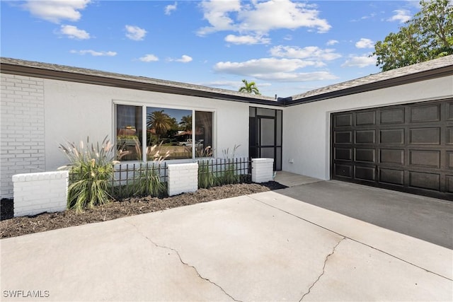 entrance to property featuring an attached garage, brick siding, driveway, and stucco siding