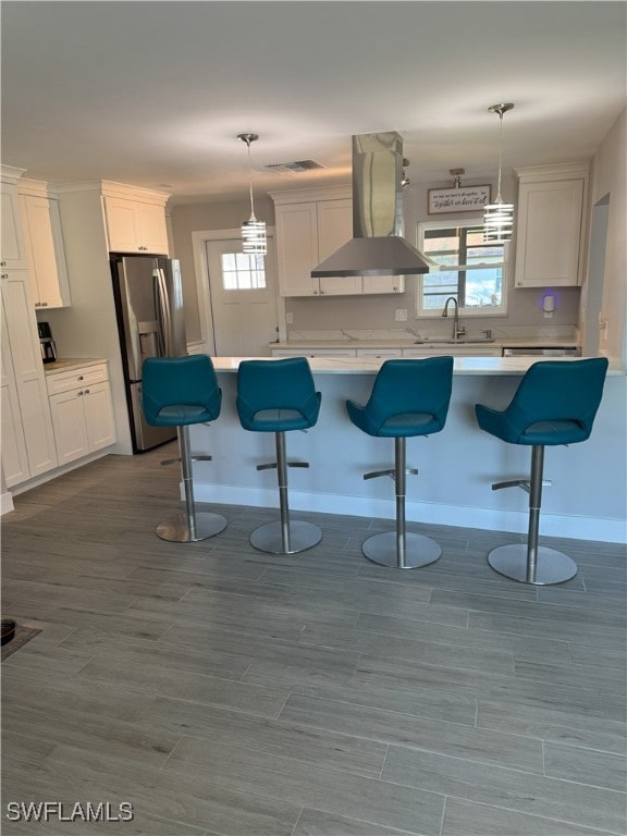 kitchen featuring island exhaust hood, a sink, a breakfast bar area, white cabinets, and stainless steel fridge with ice dispenser