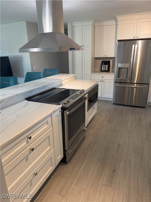 kitchen with ventilation hood, appliances with stainless steel finishes, white cabinets, light wood finished floors, and light stone countertops