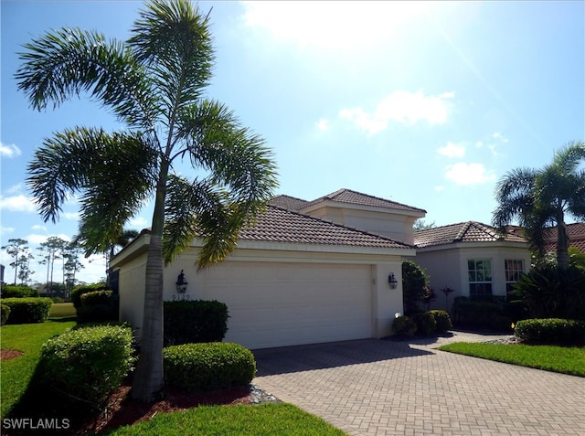 view of front of home featuring stucco siding, an attached garage, a tile roof, and decorative driveway