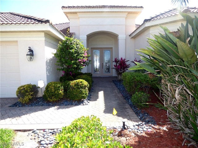 doorway to property with a tiled roof, stucco siding, french doors, and an attached garage