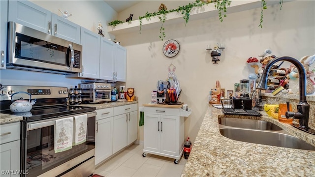 kitchen with a sink, appliances with stainless steel finishes, light stone countertops, and light tile patterned flooring