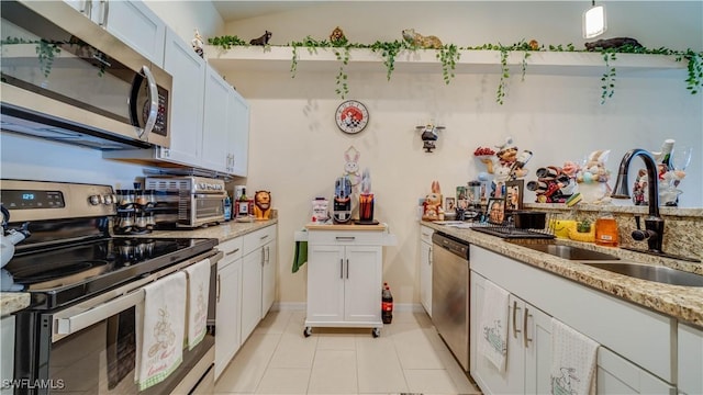 kitchen with a sink, white cabinetry, light stone countertops, appliances with stainless steel finishes, and light tile patterned floors