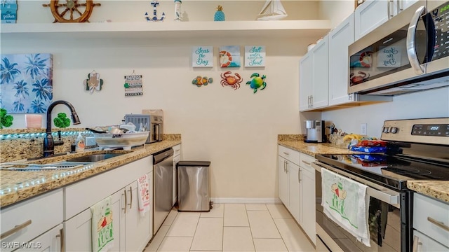 kitchen featuring white cabinetry, light tile patterned floors, stainless steel appliances, a sink, and light stone countertops