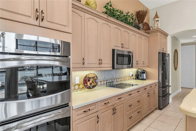 kitchen with backsplash, light countertops, light tile patterned floors, appliances with stainless steel finishes, and arched walkways