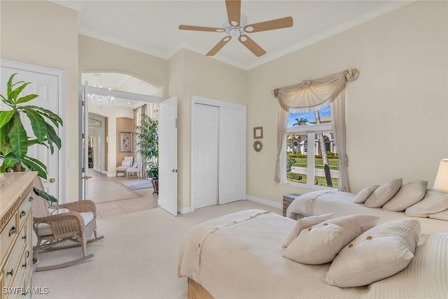 bedroom featuring ceiling fan, baseboards, ornamental molding, light carpet, and a closet