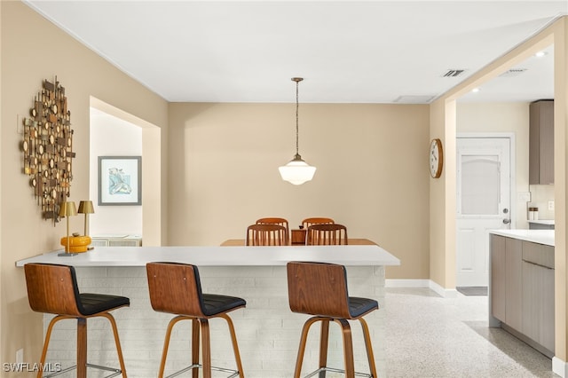 kitchen with visible vents, baseboards, decorative light fixtures, a kitchen bar, and light speckled floor