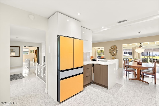 kitchen featuring visible vents, a peninsula, freestanding refrigerator, light speckled floor, and white cabinetry