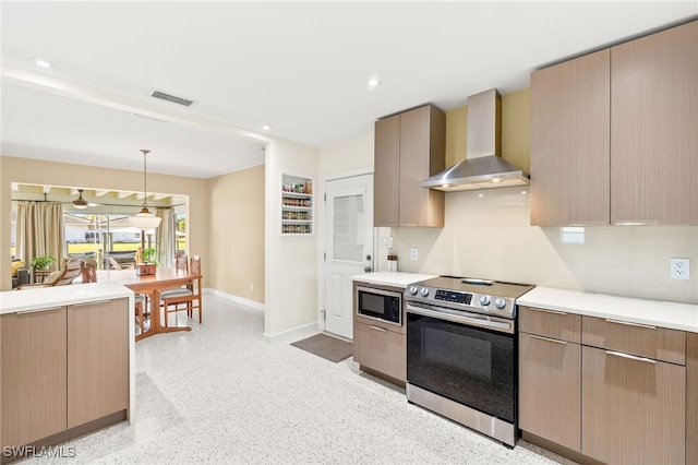 kitchen with baseboards, wall chimney range hood, light countertops, hanging light fixtures, and stainless steel appliances