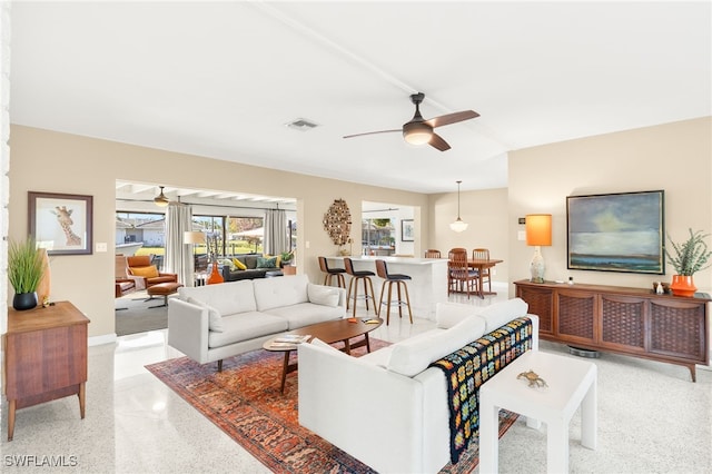 living area with baseboards, visible vents, light speckled floor, and ceiling fan