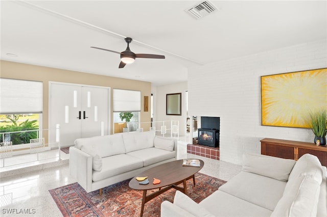 living room with visible vents, brick wall, a wood stove, and a ceiling fan