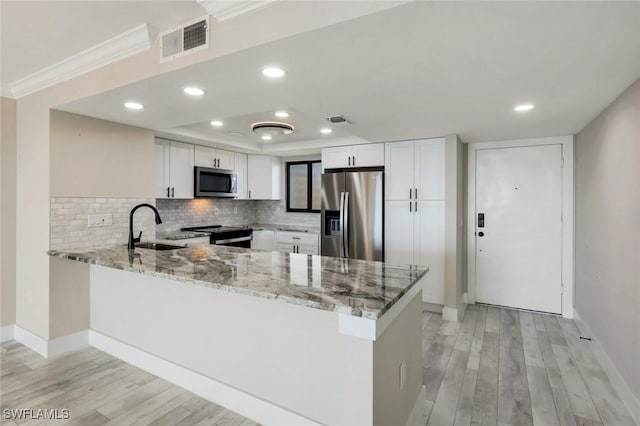 kitchen with light stone countertops, visible vents, a peninsula, a sink, and appliances with stainless steel finishes