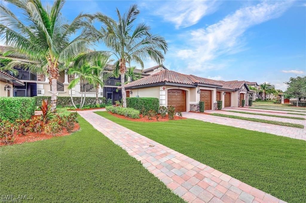 mediterranean / spanish-style home featuring driveway, stucco siding, a front lawn, a garage, and a tile roof