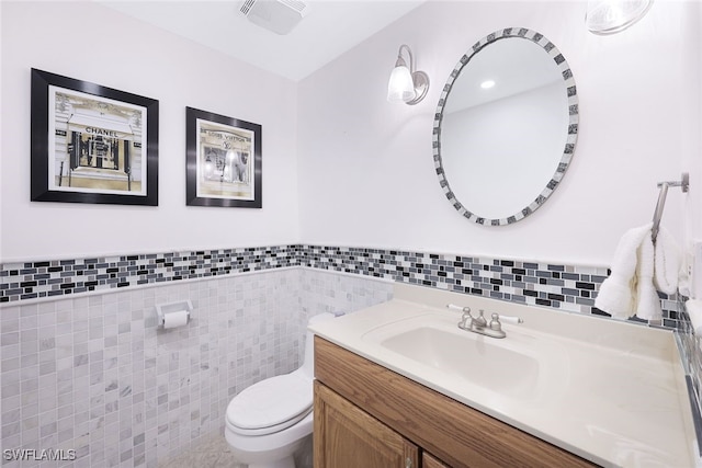 half bathroom with visible vents, a wainscoted wall, toilet, vanity, and tile walls