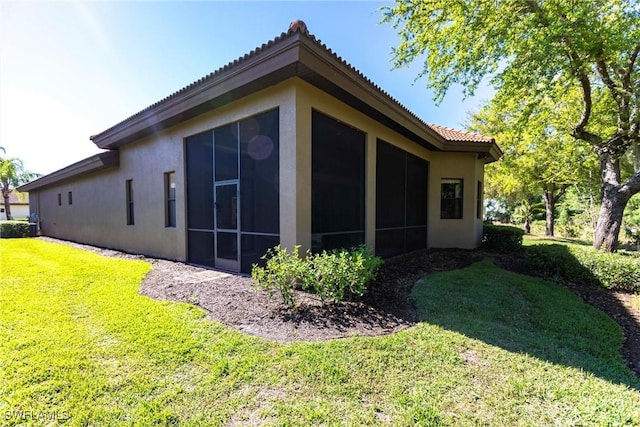 view of property exterior with a tiled roof, stucco siding, a yard, and a sunroom