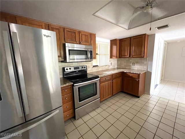4703 SE 17th Pl Unit 105, Cape Coral, FL 33904 - kitchen with stainless steel appliances, light tile patterned flooring, backsplash, brown cabinetry, and light stone counters