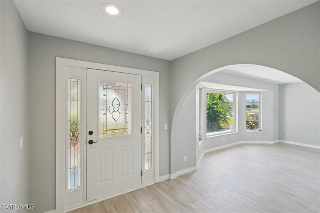 entryway featuring light wood-type flooring, arched walkways, and baseboards