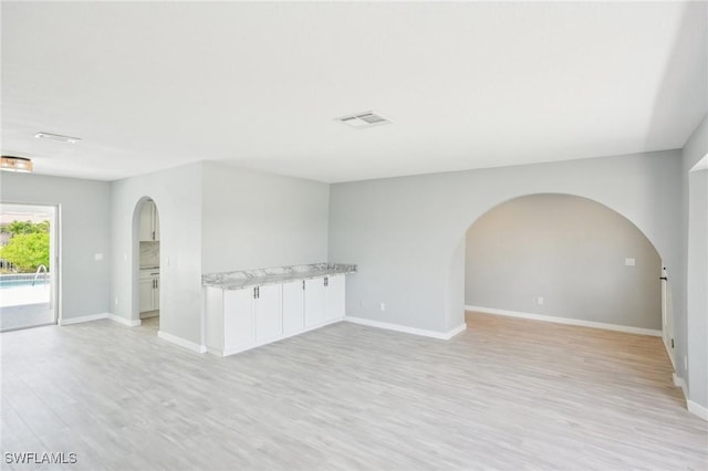 spare room with visible vents, arched walkways, light wood-style floors, and baseboards