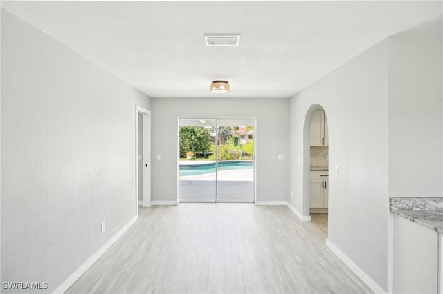 unfurnished room featuring arched walkways, visible vents, baseboards, and light wood-style floors