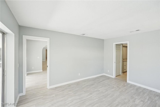 empty room featuring light wood-style flooring, baseboards, and arched walkways