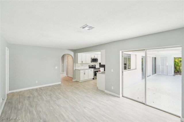 unfurnished living room featuring arched walkways, visible vents, plenty of natural light, and light wood-style floors