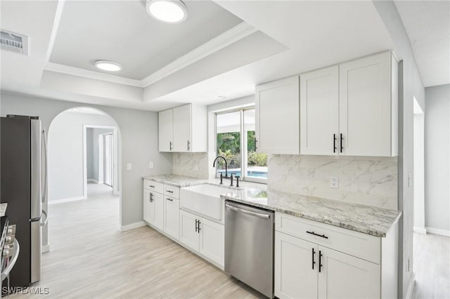 kitchen featuring arched walkways, a sink, stainless steel appliances, a raised ceiling, and backsplash