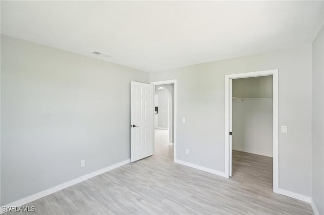 unfurnished bedroom featuring a spacious closet, visible vents, light wood-type flooring, and baseboards