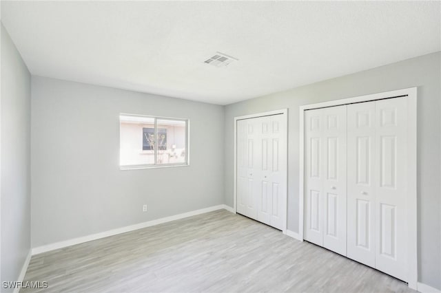 unfurnished bedroom with visible vents, two closets, baseboards, and wood finished floors