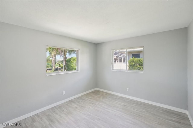 empty room with a wealth of natural light, baseboards, and wood finished floors