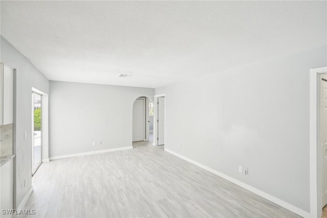 unfurnished room with baseboards, arched walkways, light wood-style floors, and visible vents