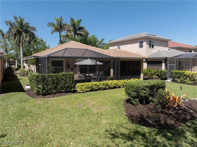 rear view of house featuring glass enclosure, a tile roof, a yard, and stucco siding