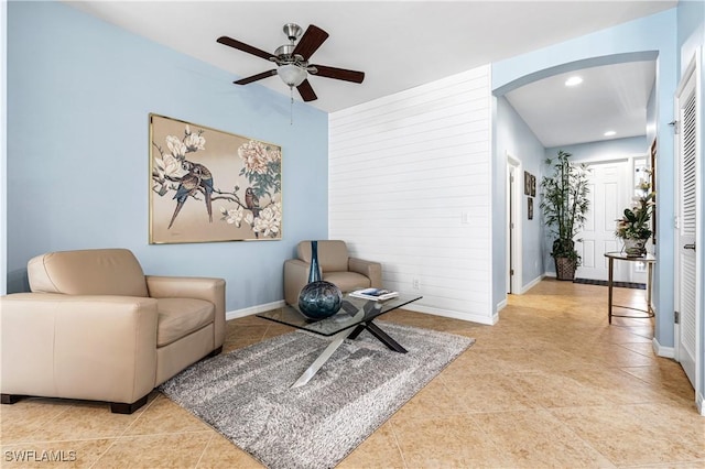 living area with tile patterned floors, baseboards, arched walkways, and a ceiling fan