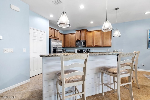 kitchen with visible vents, appliances with stainless steel finishes, a breakfast bar area, brown cabinetry, and light stone countertops