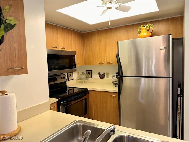 kitchen featuring light countertops, a skylight, brown cabinetry, stainless steel appliances, and a ceiling fan