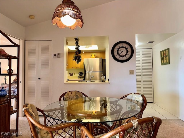 carpeted dining room with tile patterned floors, visible vents, and lofted ceiling