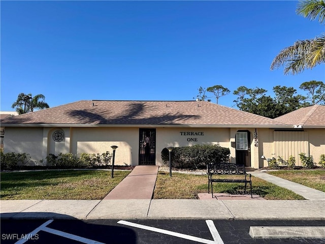 view of front of home featuring stucco siding, a front lawn, and roof with shingles