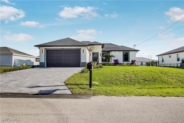 prairie-style house featuring a front yard, fence, driveway, an attached garage, and stucco siding