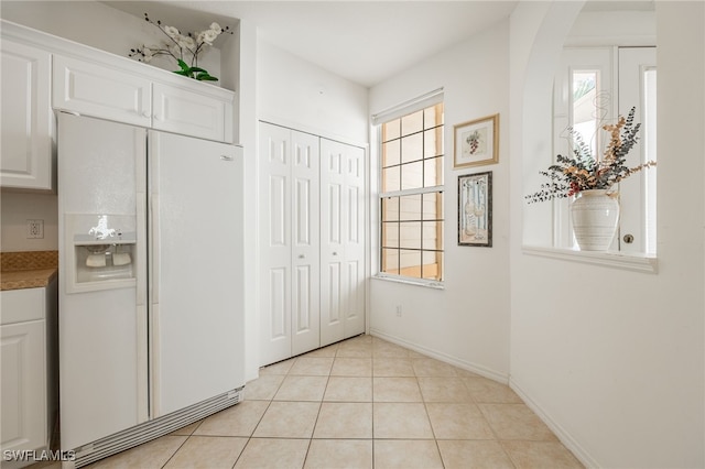 kitchen featuring white cabinetry, white refrigerator with ice dispenser, plenty of natural light, and light tile patterned floors