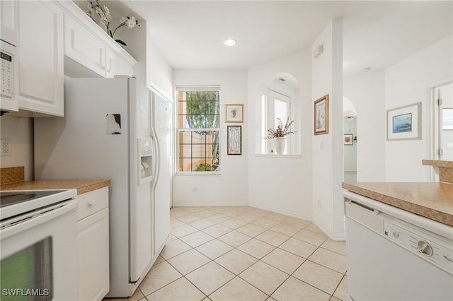 kitchen featuring white appliances, light tile patterned floors, baseboards, arched walkways, and white cabinetry