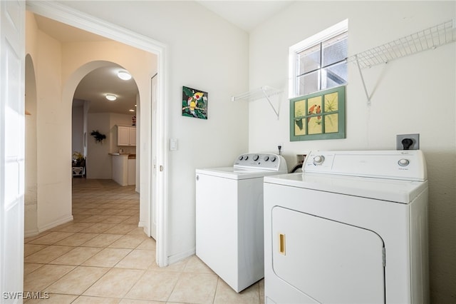 washroom featuring baseboards, laundry area, light tile patterned flooring, arched walkways, and washing machine and dryer