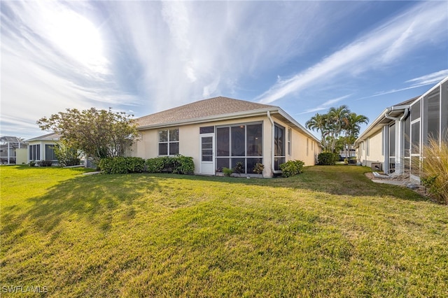 rear view of property with a yard, a sunroom, and stucco siding